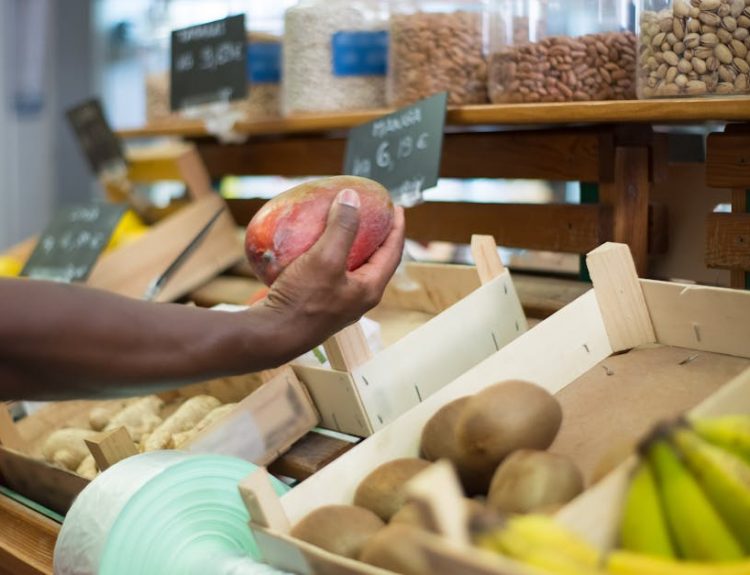 Close-up of a hand choosing a mango among fresh produce at a market in Portugal.