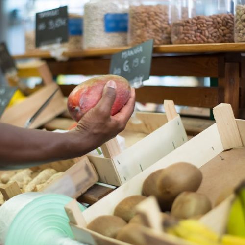 Close-up of a hand choosing a mango among fresh produce at a market in Portugal.