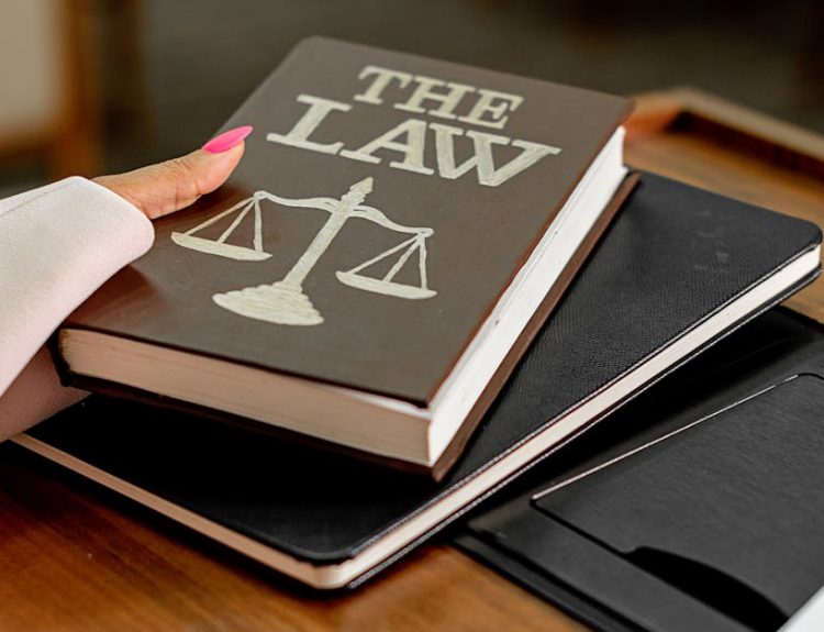 Closeup image of a law book titled 'The Law' on a wooden desk with scales of justice.