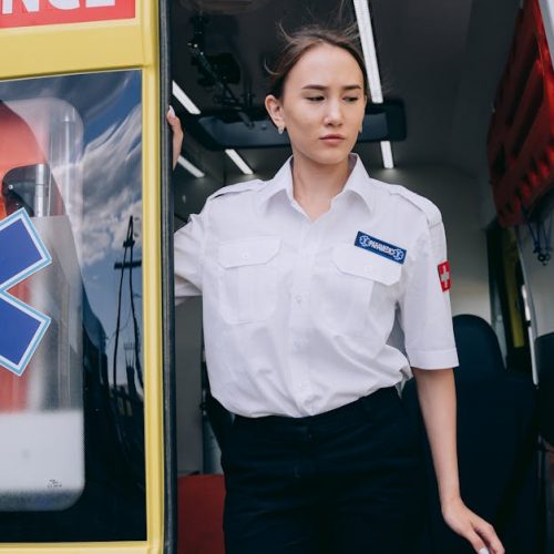 A female paramedic in uniform steps out of a yellow ambulance, ready for action.