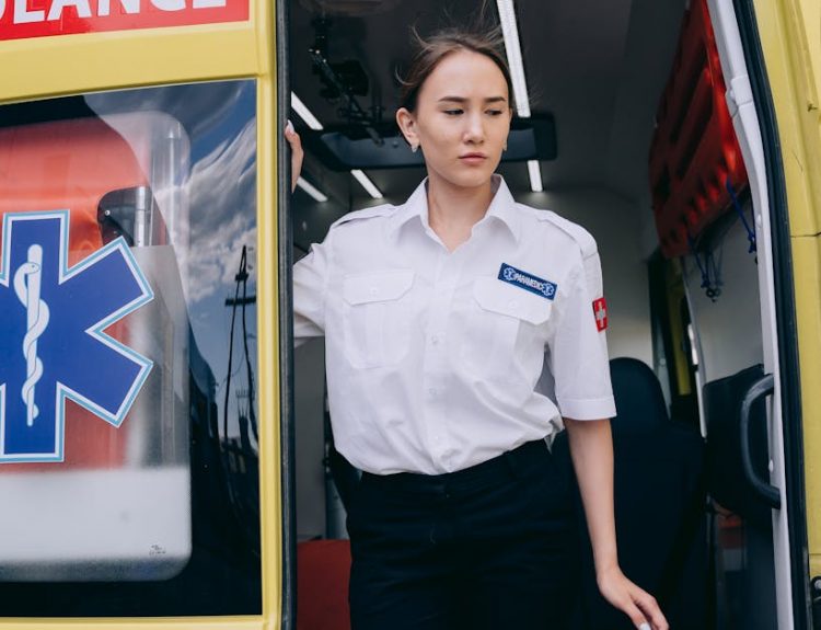 A female paramedic in uniform steps out of a yellow ambulance, ready for action.
