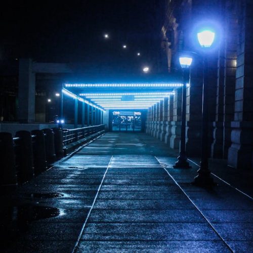 A moody, illuminated pathway at a train station during night with glowing lamps.