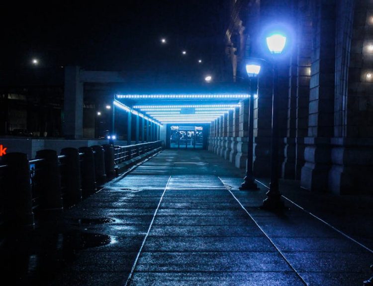 A moody, illuminated pathway at a train station during night with glowing lamps.