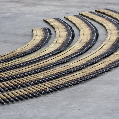 Curved rows of bullets aligned meticulously on a concrete floor, creating a pattern.