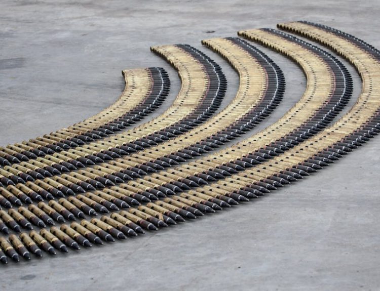 Curved rows of bullets aligned meticulously on a concrete floor, creating a pattern.