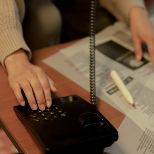 Woman using a landline and newspaper for a job search, highlighting domestic life.