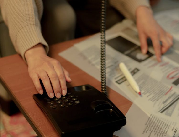 Woman using a landline and newspaper for a job search, highlighting domestic life.