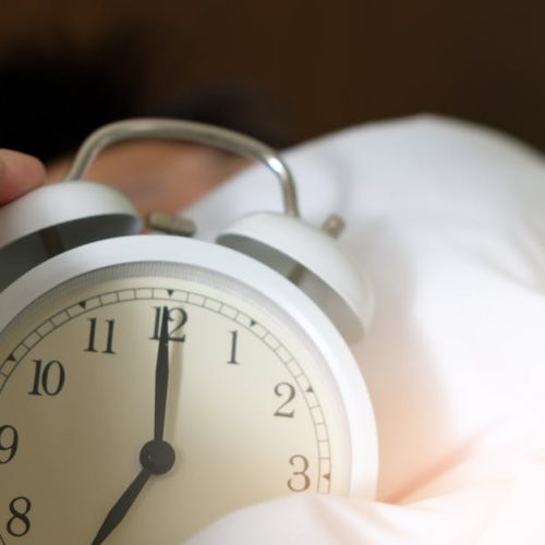 A close-up of a hand reaching for a ringing alarm clock, symbolizing waking up in the morning.