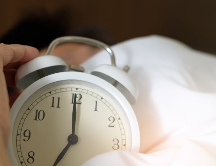 A close-up of a hand reaching for a ringing alarm clock, symbolizing waking up in the morning.