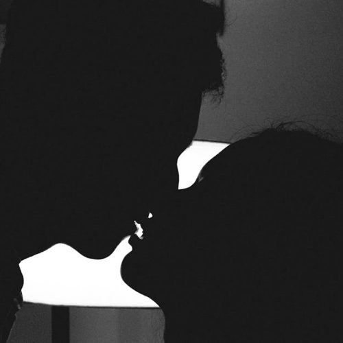 Silhouette of a couple kissing in a romantic and intimate moment against a bright light.