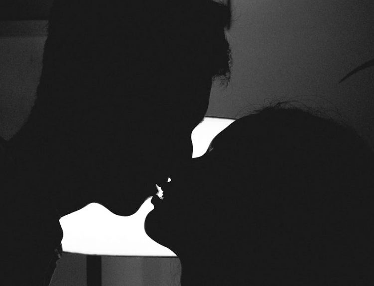 Silhouette of a couple kissing in a romantic and intimate moment against a bright light.