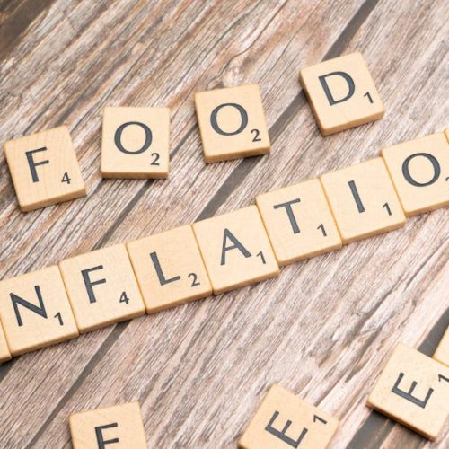 Wooden scrabble tiles arrange to spell 'Food Inflation' on a rustic wooden surface, conceptually depicting rising food prices.