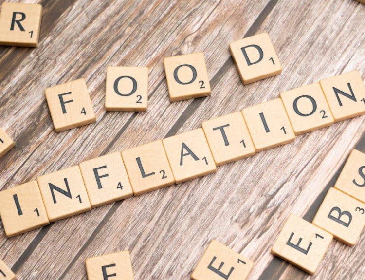 Wooden scrabble tiles arrange to spell 'Food Inflation' on a rustic wooden surface, conceptually depicting rising food prices.