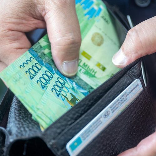 Person handling Kazakhstani tenge banknotes from a wallet, close-up view.