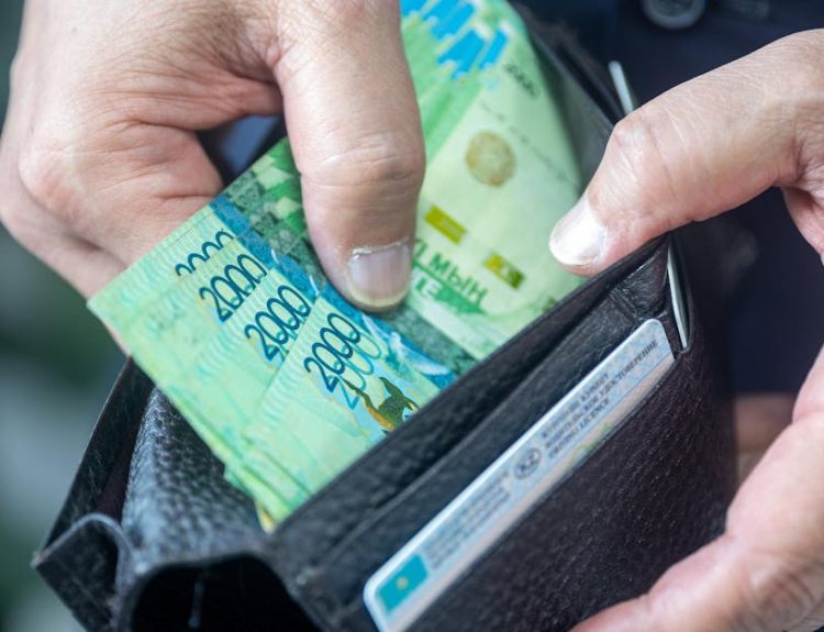 Person handling Kazakhstani tenge banknotes from a wallet, close-up view.