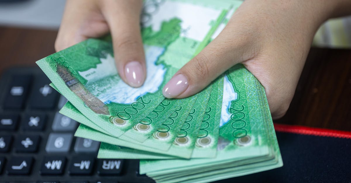Close-up of hands counting Kazakhstani tenge bills beside a keyboard.