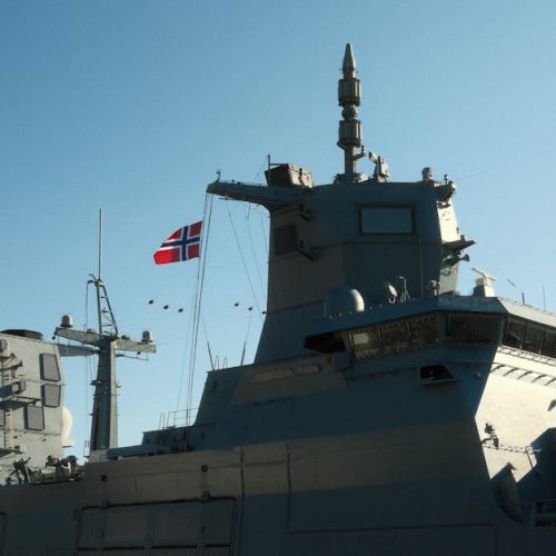 A Norwegian navy frigate with a national flag in daylight.
