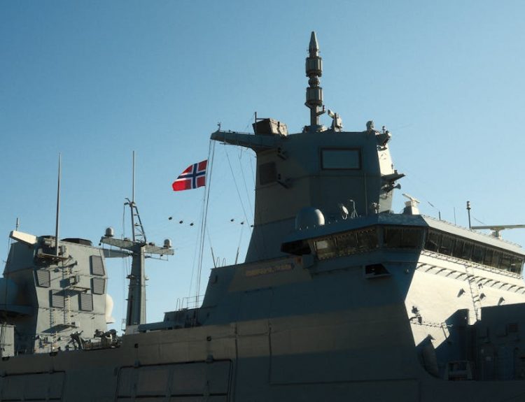 A Norwegian navy frigate with a national flag in daylight.