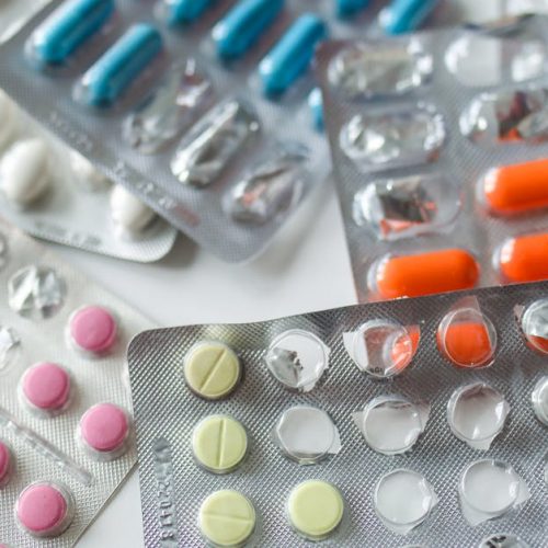 Assorted colorful blister packs of pills and capsules on a white surface.
