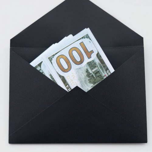 Hundred dollar bills partially visible in an open black envelope on a white background.