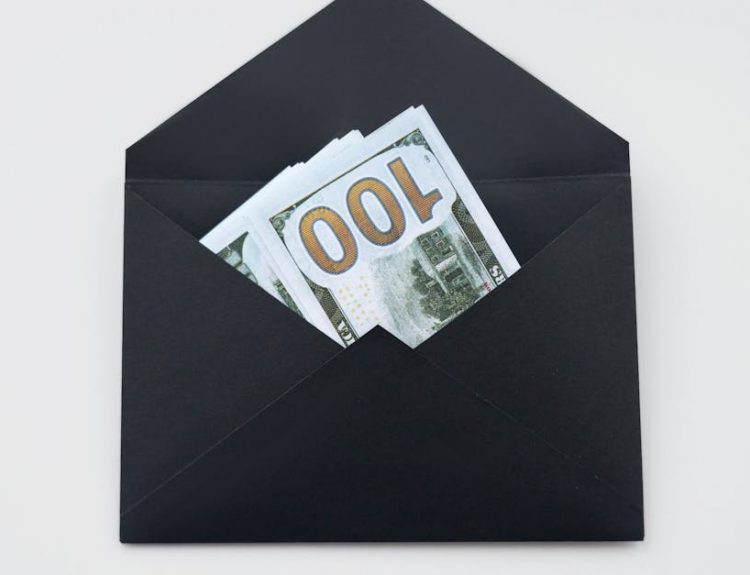 Hundred dollar bills partially visible in an open black envelope on a white background.