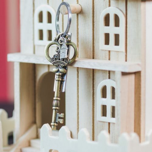 Miniature wooden house with a vintage key, symbolizing real estate and homeownership.