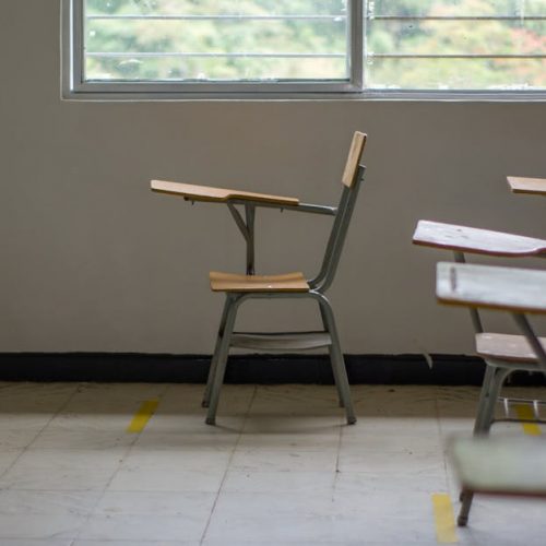 Quiet empty classroom interior with school desks by a large window.