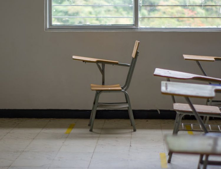 Quiet empty classroom interior with school desks by a large window.