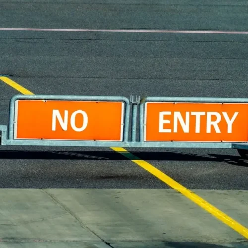 A warning sign indicating no entry on an airport taxiway with a bold yellow line.
