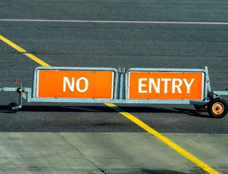 A warning sign indicating no entry on an airport taxiway with a bold yellow line.