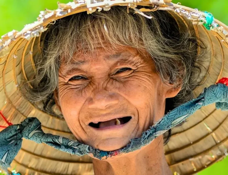 A vibrant portrait of a smiling elderly woman in a conical hat against a green background.