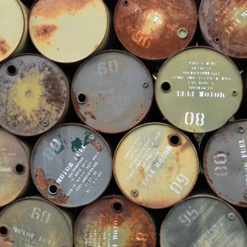 Pile of old, rusty oil barrels stacked outdoors with visible labels and numbers.