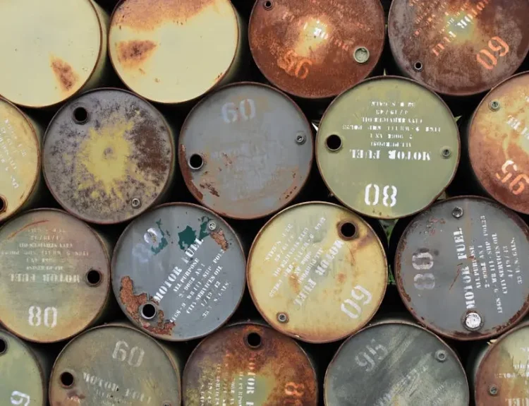 Pile of old, rusty oil barrels stacked outdoors with visible labels and numbers.