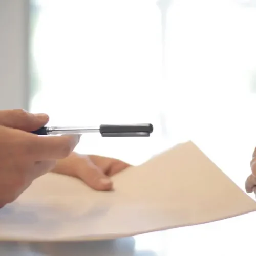 Close-up of a contract signing with hands over documents. Professional business interaction.